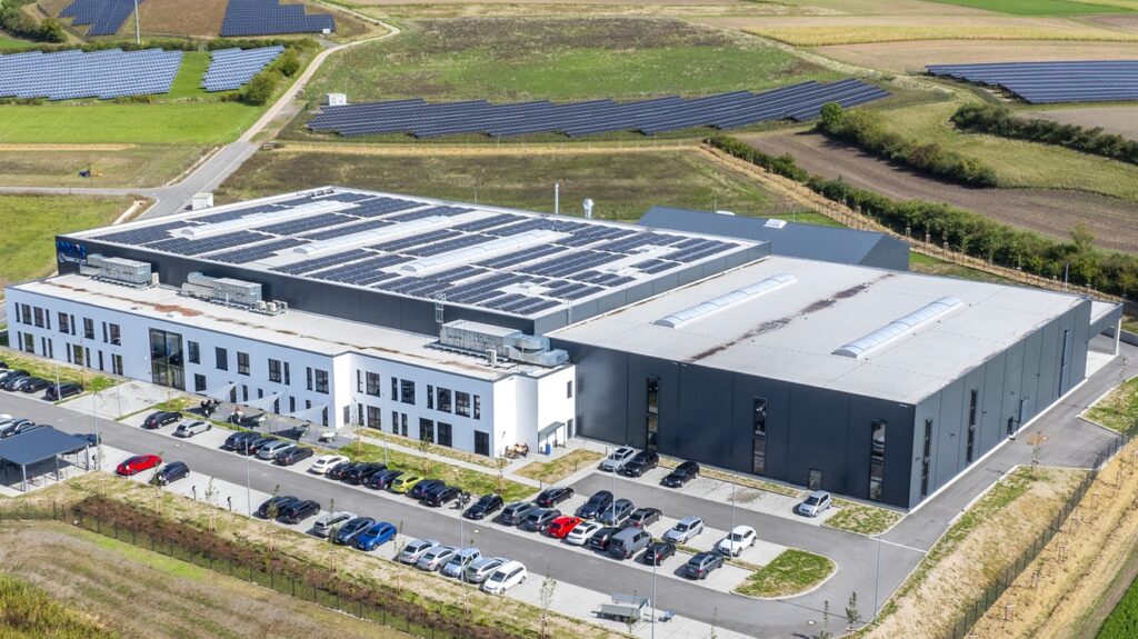 Vogelperspektive auf das UNICOR Betriebsgelände mit Büro- und Produktionsgebäuden, Parkplätzen, Zufahrtswegen und Grünflächen.